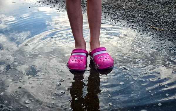 Feet of child in pink shoes standing in a puddle in the rain