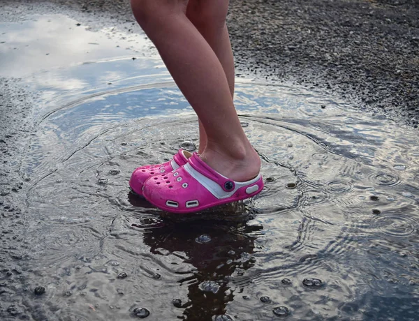 Pés de criança em sapatos rosa em pé em uma poça na chuva — Fotografia de Stock