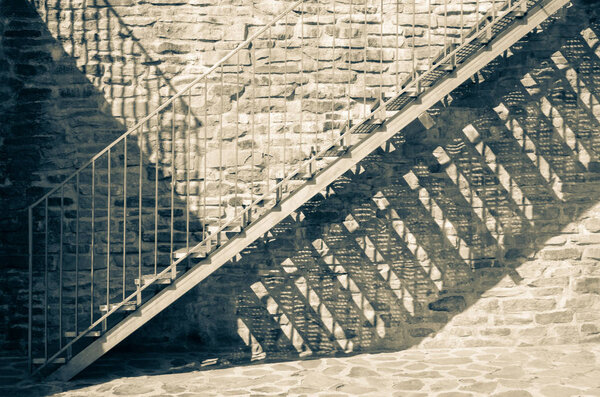 Metal stairs with shadows on stone wall