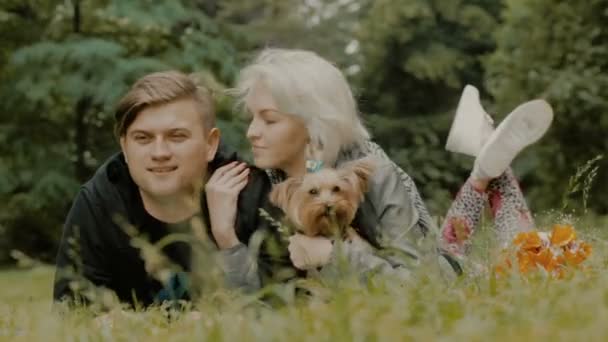 Shot of a young couple with a dog. They lie on the grass — Stock Video