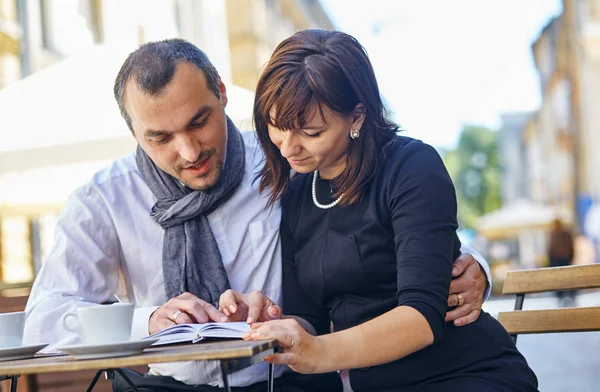 Young couple reading a book in a cafe on the street — Stock Photo, Image