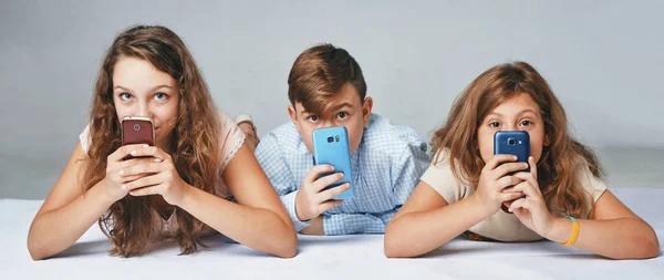 Niños se esconden detrás de los teléfonos —  Fotos de Stock