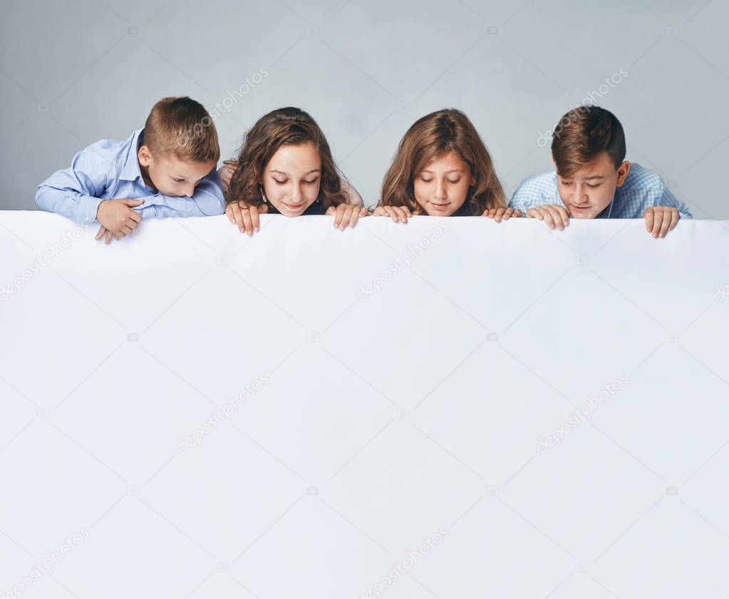 a Four children holding a big billboard, looking down on it.
