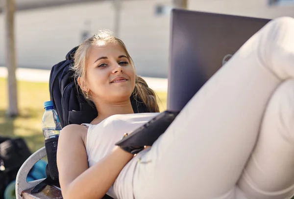 Mujer rubia joven miente, disfruta del día de verano, bloggs y chats a través de un teléfono inteligente, usa tonos de moda, tiene una sonrisa positiva, se recrea durante las vacaciones. Concepto de personas y estilo de vida . — Foto de Stock