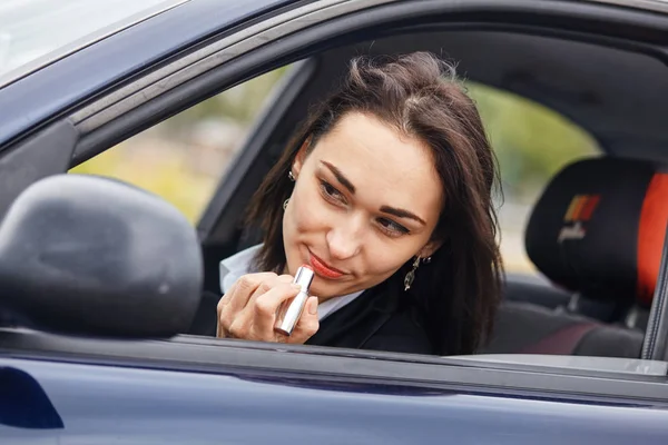 Jeune femme appliquant du rouge à lèvres pendant la conduite . — Photo