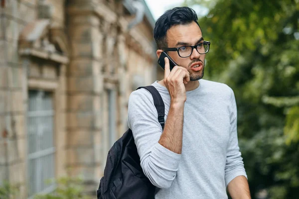 Portrét pohledný muž student venku na univerzitní kampus a mluví o mobilní telefon, kopírování prostor. Sebevědomý a úspěšný student. Koncepce vzdělávání, cestování a cestovní ruch — Stock fotografie