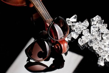 Sunglasses, violin, pieces of ice on a glass background