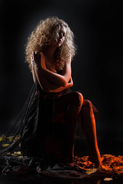 Молодая обнаженная женщина и желтые осенние листья на фоне студии