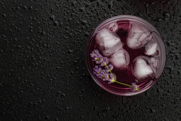 Lavender lemonade with ice on wet black background.
