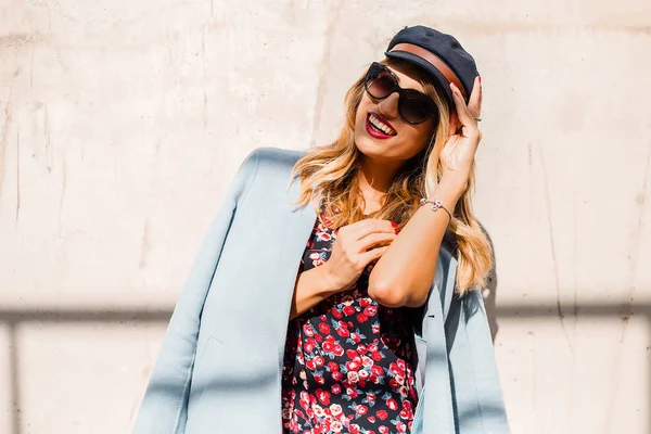 Güneş gözlüğü ve duvar dibinde poz parlak elbise giyen çekici genç sarışın kadın
