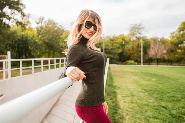 魅力的な金髪女性サングラスと公園の手すりでポーズ — ストック写真