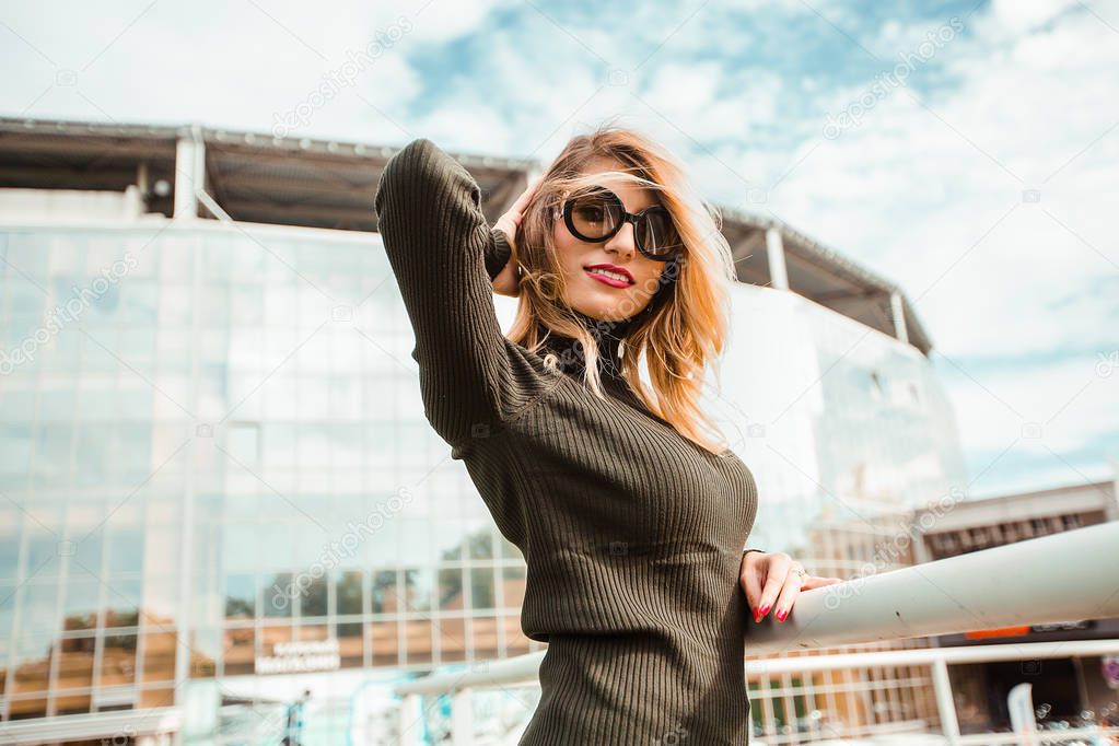 Attractive young blonde woman wearing sunglasses and posing in modern city