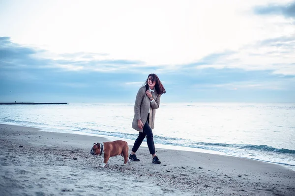 Pretty woman walking with dog at sea in cold weather at dusk