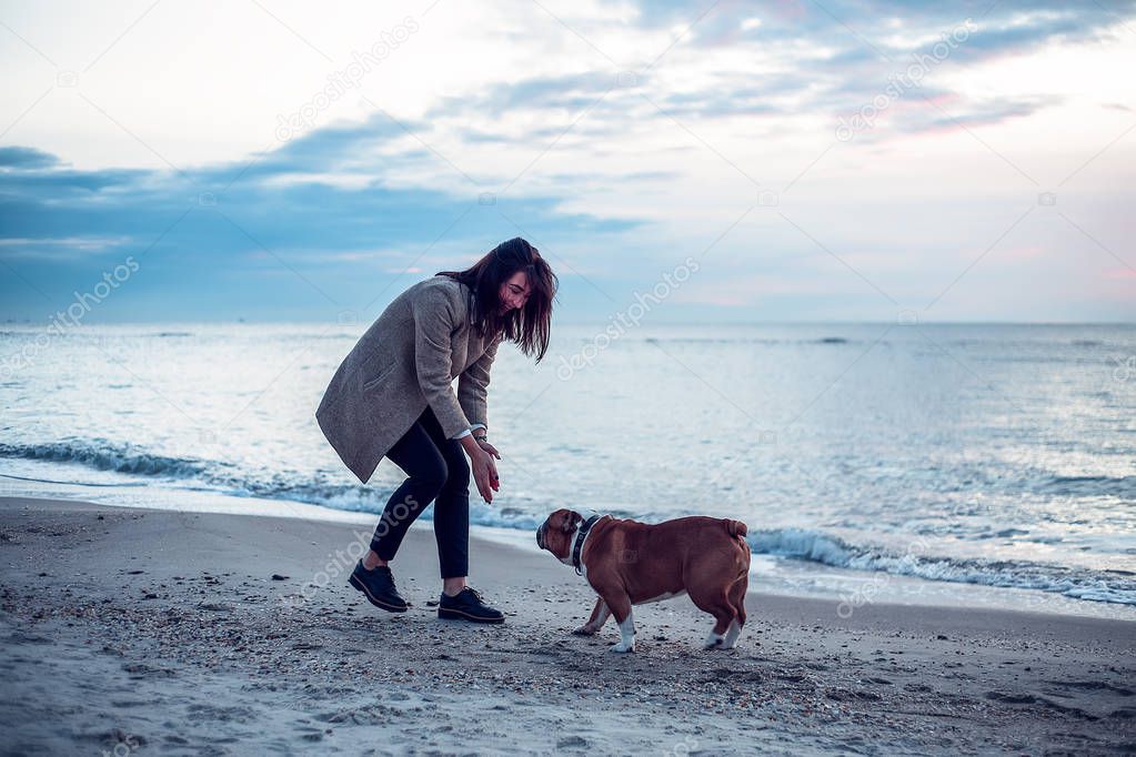 Pretty woman walking with dog at sea in cold weather at dusk