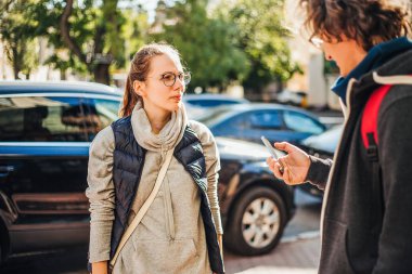 Genç turist çift ayakta açık havada gündüz, Park yakınındaki. Adam holding smartphone elinde