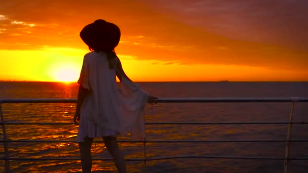 年轻漂亮的女人穿着白色的礼服和帽子摆在海上背景在惊人的日落 — 图库视频影像