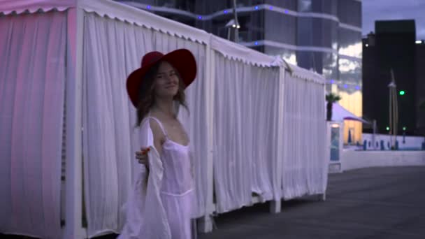 白いドレスと白いテント背景アウトドアで踊る赤い帽子を身に着けている魅力的なブルネットの女性 — ストック動画