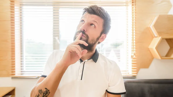 thoughtful bearded man with facial expression putting finger on mouth