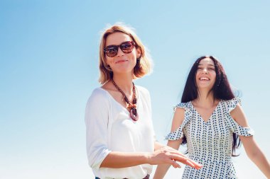 Açık eğlenceli iki mutlu genç kadın portresi mavi gökyüzü ve denizin özgeçmişlerine poz