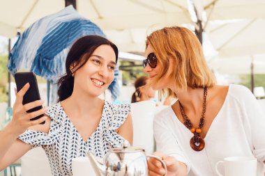 açık kafede masada oturan smartphone kullanarak iki genç kadın 