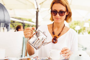 Çay Kupası holding çaydanlık açık kafede masada oturan içine dökme şık sarışın kadın