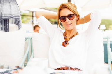 Şık sarışın kadın saçlarını açık kafede masada oturan dokunmadan güneş gözlüğü takıyor