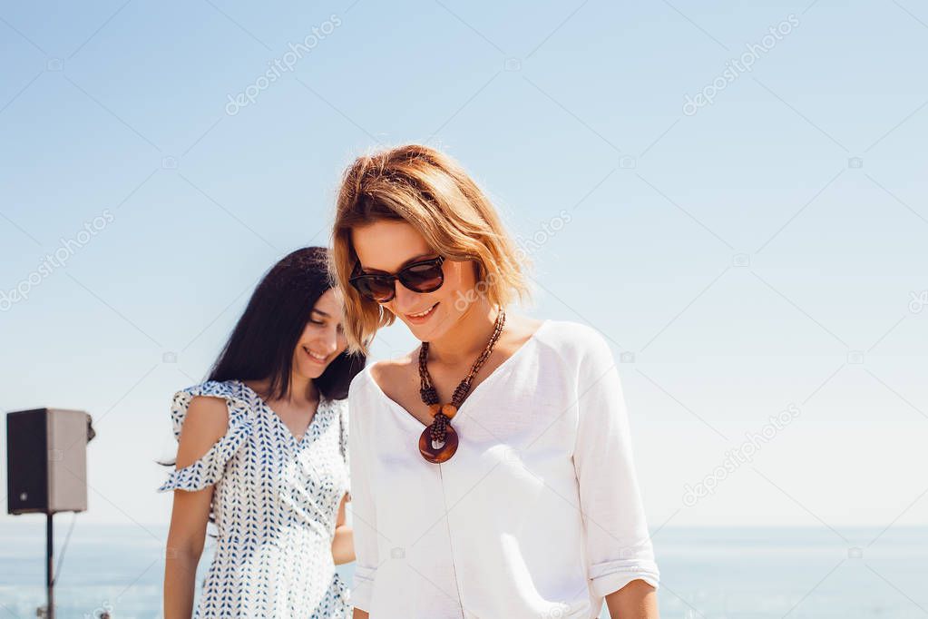 outdoor portrait of two happy young women having fun posing on blue sky and sea background