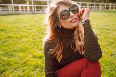 Park yeşil çimenlerin üzerinde oturan güneş gözlüğü takıyor gülümseyen genç kadın portresi 