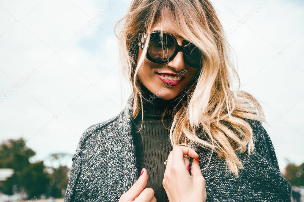 happy young woman with grey coat and sunglasses smiling posing in park 
