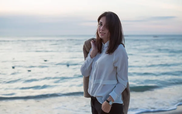 three quarter length portrait of stylish brunette woman with grey coat posing sea background