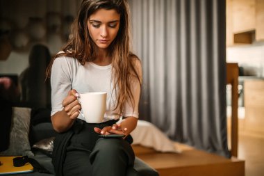 beyaz kahve fincanı tutarak ve kapalı oturma smartphone kullanarak kadın