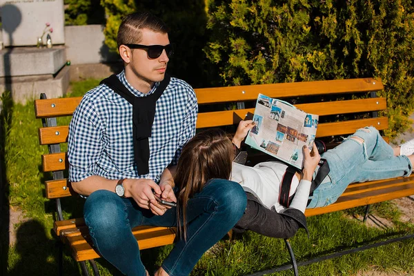年轻女子躺在男友的膝盖和阅读小册子在公园板凳上 — 图库照片