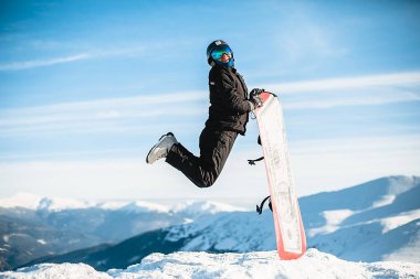 Happy man jumps with snowboard in mountains 