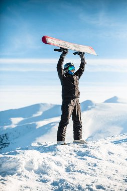Guy holds a snowboard over his head in the mountains
