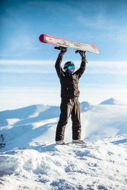Guy holds a snowboard over his head in the mountains