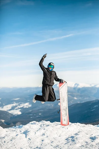 Happy man jumps with snowboard in mountains