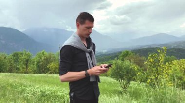 Yaz günü dağların arasında yürürken akıllı telefon kullanan sıradan giyinmiş yakışıklı bir adam.