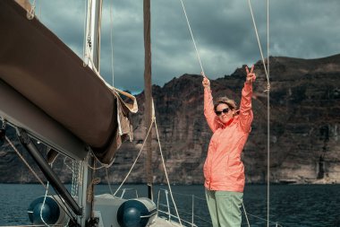 Güneşli bir günde yatta dinlenen sıcak elbiseli mutlu bir kadın.
