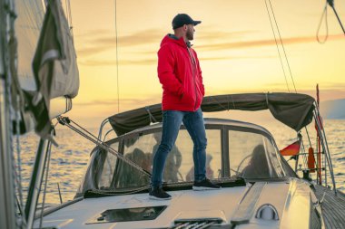 Sıcak elbiseli sakallı adam güneşli bir günde yatta dinleniyor.