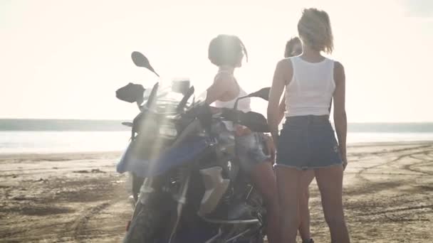 krásné sexy ženy v letním oblečení baví při stání v blízkosti motocyklu na pláži 