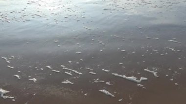 Kumlu plajda beyaz köpük oluşturan deniz dalgaları