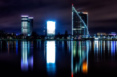 Riga gökdelenleri olan bir gökyüzü. Daugava nehir sularında manzaralı su yansımaları ile gece çekimi.