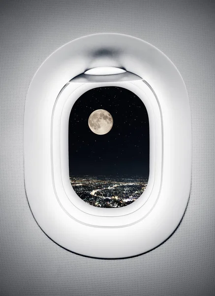 Night city under moon at airplane window