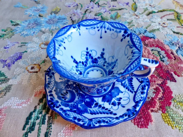 Cup with saucer, linen tablecloth. Things in Russian traditional Gzhel style. Closeup. Gzhel - Russian folk craft of ceramics and production porcelain and a kind of Russian folk painting.