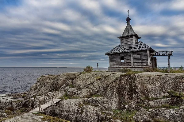 Old chapel on the shore of Lake Ladoga. The blue sky and the water surface of the lake. Severe nature of the Russian north. Landscape