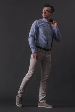 Tam boy görüntü akıllı rahat kıyafetler ve ceketini basılı tutup, gri arka plan üzerinde seyir gözlük yakışıklı genç işadamı