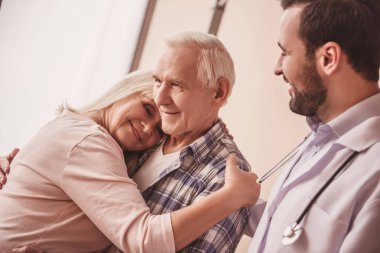 Güzel yaşlı çift sarılma ve gülümseyen, Doktor onlara bakmak mutlu