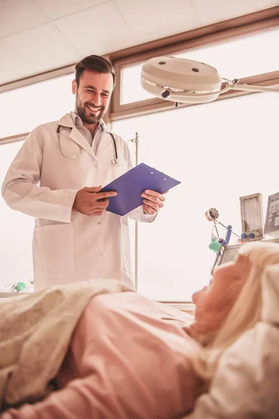Pohledný Doktor Dívá Jeho Manželka Leží Posteli Nemocniční Oddělení Usmívá — Stock fotografie