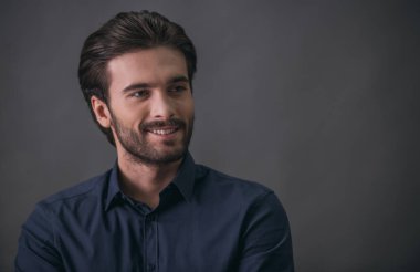 Yakışıklı emin işadamı kıl, koyu mavi gömlek ile uzağa bakarak ve, gri arka plan üzerinde gülümseyen