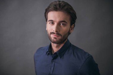 Yakışıklı emin işadamı ile kıl, kamera, gri arka plan üzerinde koyu mavi gömlek bakıyor